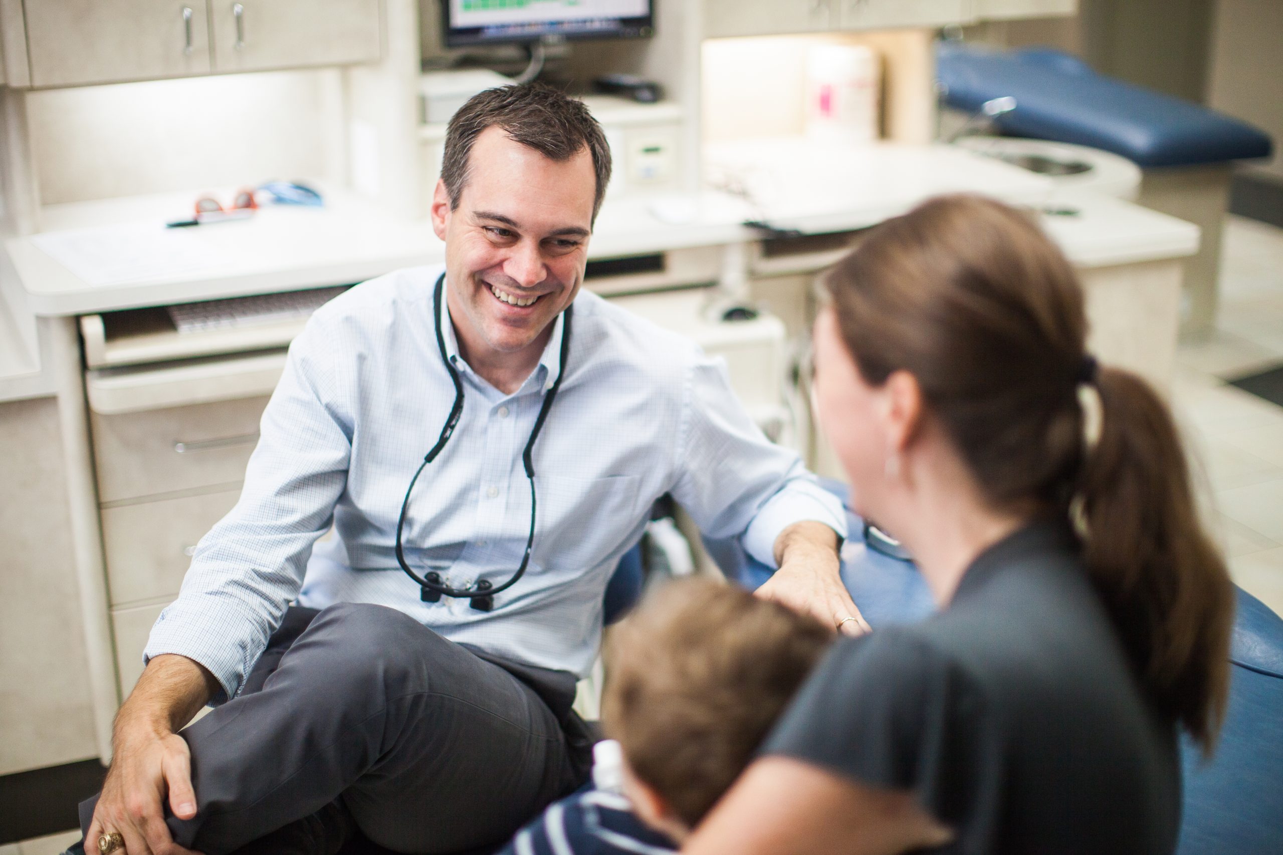 Dentist smiling with a young child and parent during a friendly visit